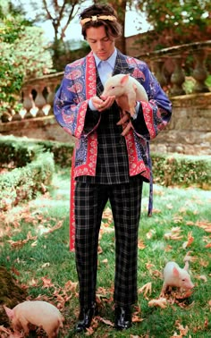 a man standing in the grass holding a small dog and wearing a jacket with an animal print on it