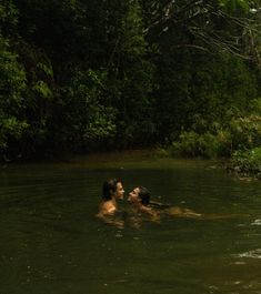 two people are swimming in the water near some trees and bushes, one is kissing the other