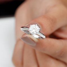 a woman's hand holding an engagement ring with a diamond in the middle, on top of her finger