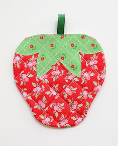 an apple shaped pot holder with green leaves and pink flowers on red quilted material