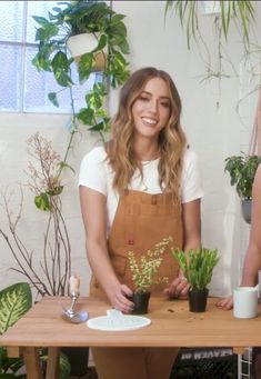 two women standing behind a table with potted plants