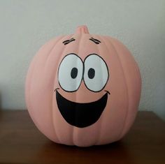 a pink pumpkin with a smiley face painted on it's side sitting on a table