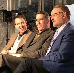 three men sitting next to each other in front of a tv screen and camera equipment