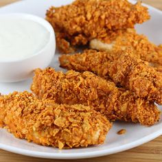 some fried food on a white plate next to a small bowl of ranch dressing and dipping sauce