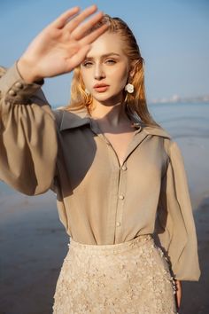 a woman is standing on the beach with her hand up to her face and wearing a dress