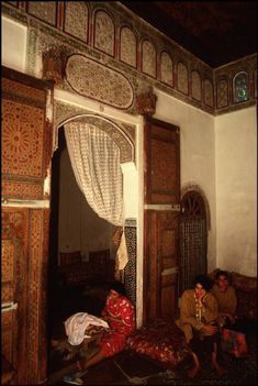 two people sitting on the floor in front of an open door with curtains and drapes