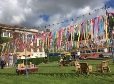 colorful streamers hang over tables and chairs on the grass outside an old building with a bus in the background