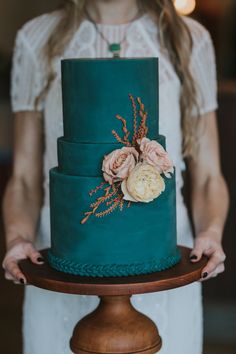 a woman is holding a green cake with flowers on the top and bottom tiers