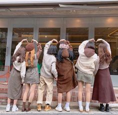 four girls standing in front of a store with their hands on their head and looking into the window