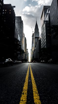 an empty city street with yellow lines painted on the road and tall buildings in the background