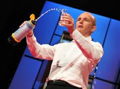 a man holding a water bottle and spraying it with a sprinkler on stage