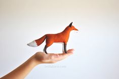 a hand holding a small toy fox on it's palm against a white background