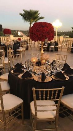 a table set up with black and white linens, gold chargers and red roses