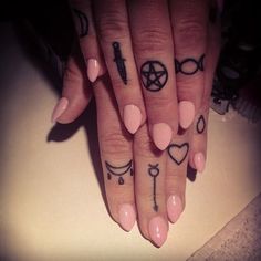 a woman's hand with tattoos on it and two fingers that have crosses, keys, hearts, and other symbols