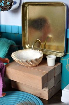 there is a doll sitting in front of a mirror with a bowl on the table next to it