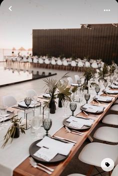 a long table is set up with white chairs and place settings for an outdoor event