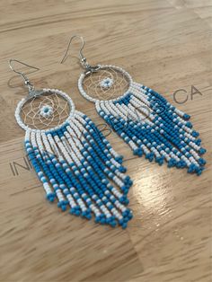 a pair of blue and white beaded earrings sitting on top of a wooden table