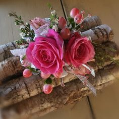 pink roses and greenery are placed on a piece of driftwood in front of a wall