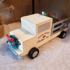 a wooden toy truck with a christmas tree on the side and a teddy bear sitting next to it