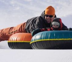 a man and child riding on an inflatable tube down the side of a snow covered slope