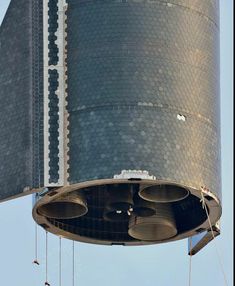 a large metal structure with bells hanging from it's sides in front of a blue sky