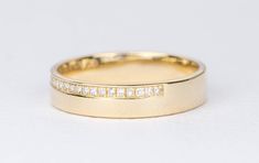 a yellow gold wedding band with channeled diamond set in the middle, on a white background