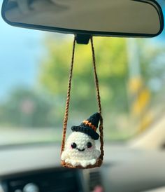 a small stuffed animal hanging from the side of a car mirror with a hat on it's head