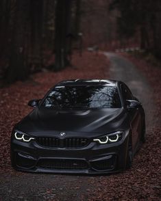 a black car parked on the side of a road in front of trees and leaves