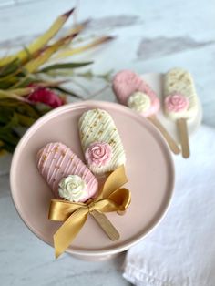 pink and white cookies on a plate with gold ribbon tied around the edges, sitting next to flowers