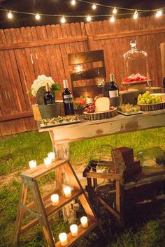 a table with candles and food on it in the grass near a fence at night