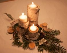 three lit candles sitting on top of a table surrounded by pine cones and other decorations