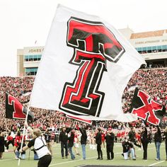 a group of people standing on top of a football field holding onto large black and red flags