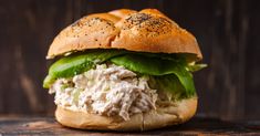 a chicken salad sandwich with lettuce and sesame seeds on a wooden table, ready to be eaten