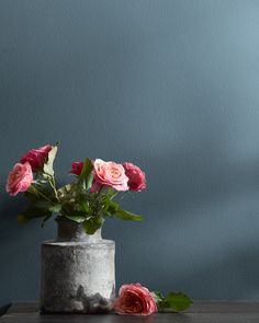 some pink roses are in a gray vase on a wooden table next to a blue wall