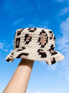 a woman's hand holding up a crocheted hat in front of a blue sky