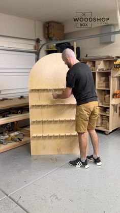 a man working on a large wooden object in a shop with shelves and tools behind him