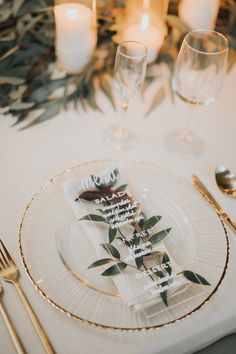 a place setting with candles and napkins on the table in front of it is decorated with greenery