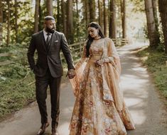 a bride and groom walking down a path in the woods holding each other's hands