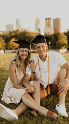 a man and woman sitting on the grass in graduation gowns smiling at the camera