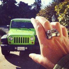 a person holding up a ring in front of a green jeep