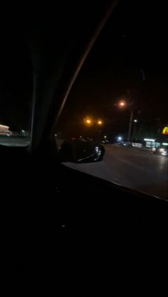 the dashboard of a car at night with street lights in the distance and cars driving down the road