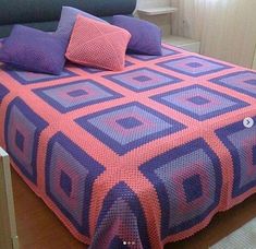 a bed with purple and pink bedspread on it in front of a window