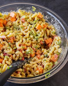 a glass bowl filled with pasta salad on top of a table next to a black spatula