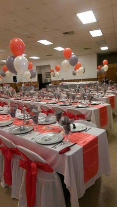 tables set up for an event with red and white tablecloths, silverware, and balloons