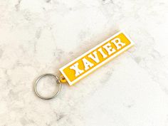 a yellow and white keychain with the word kaver on it sitting on a marble surface