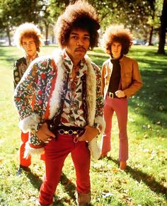 an image of three people standing in the grass with one man wearing a fur coat