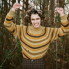 a man with his hands up in the air while standing in front of some trees