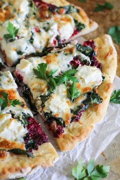 several slices of pizza with cheese and herbs on top, sitting on wax paper next to some parsley