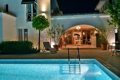 an outdoor swimming pool next to a house at night with lights on and chairs around it