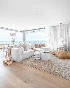 a living room filled with white furniture next to a large window covered in sheer curtains